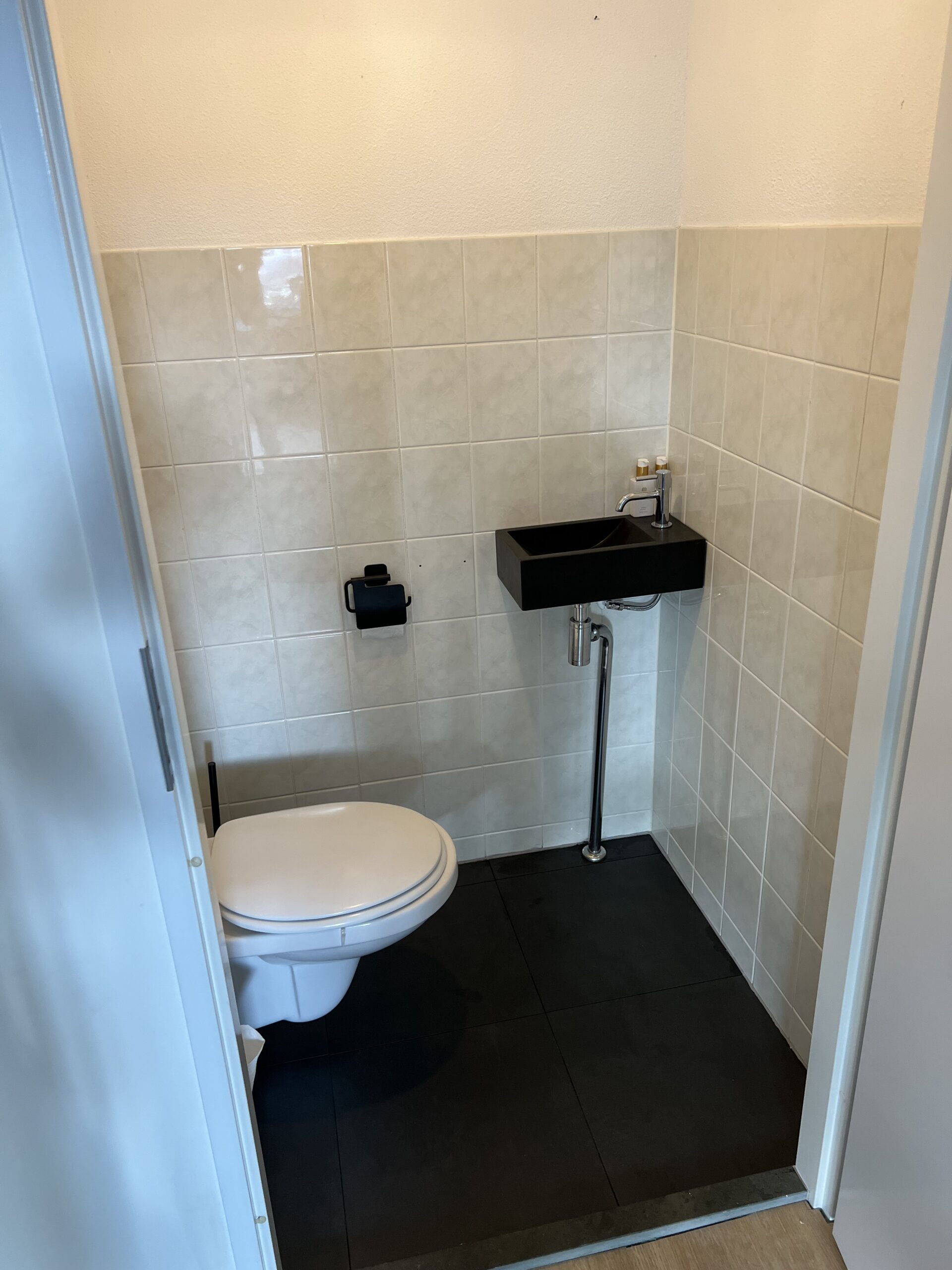 Foto na verbouwing toilet, met zwarte vloertegels en grijze tegels op de muur.