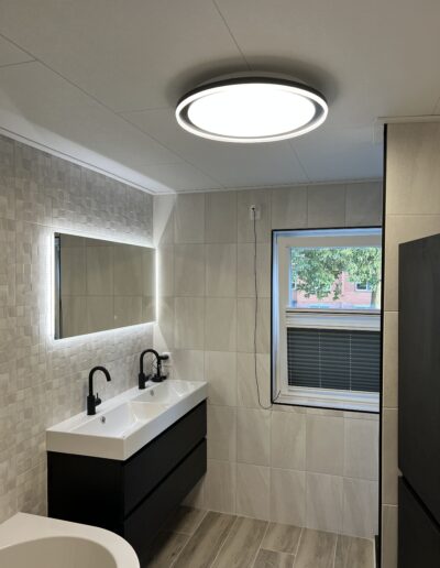 Foto badkamer na verbouwing, zwart wastafelmeubel, wit ligbad, zwarte kasten en kranen